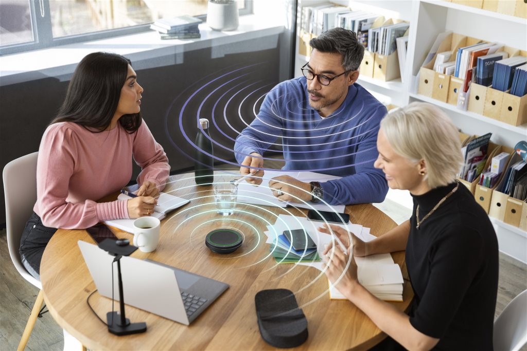 Speakerphone professionale Jabra Speak2 su un tavolo da riunione, con partecipanti impegnati in una riunione virtuale, simbolo di comunicazione aziendale chiara e produttiva.